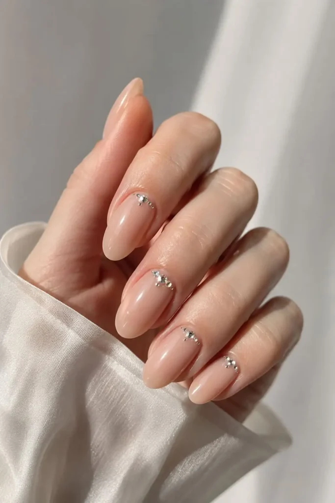 Elegant nude rhinestone nails with subtle crystals placed near the cuticles
