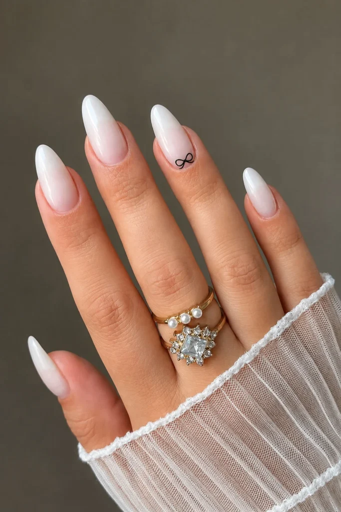 Milky white ombre almond graduation nails with a delicate black bow accent
