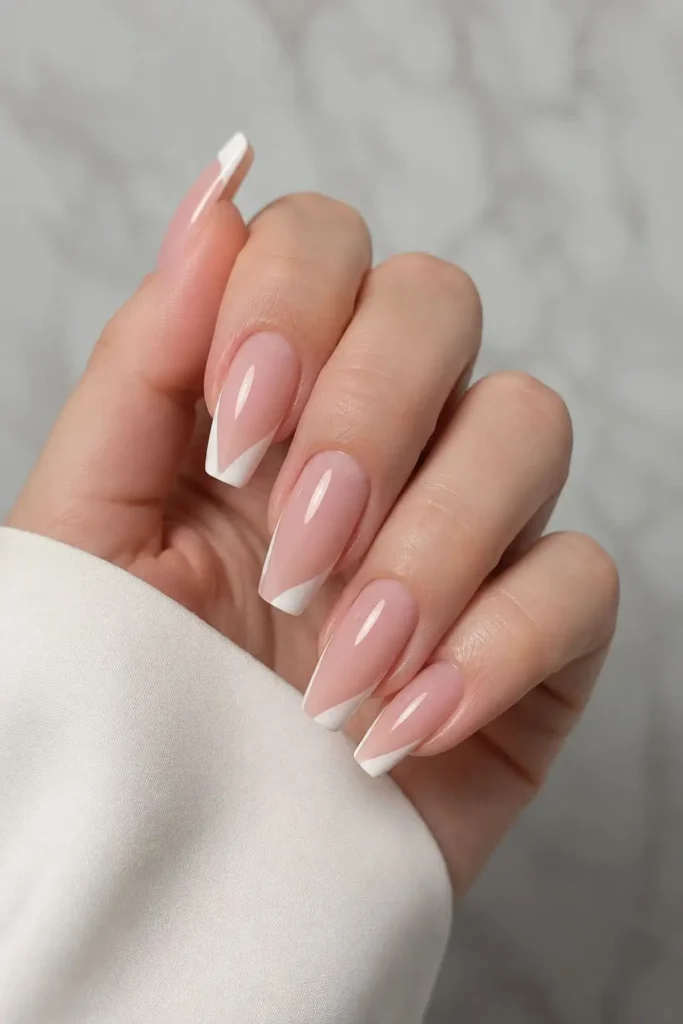 Nude French tip nails with thin white asymmetrical tips on coffin-shaped nails
