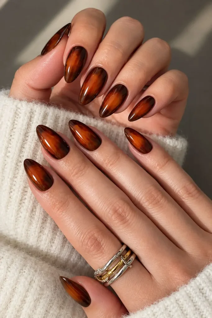 Amber aura nails with warm brown tones and a glowing orange center inspired by fall