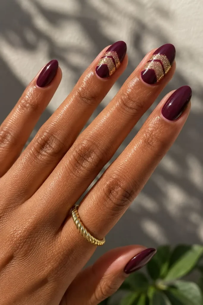 Dark burgundy nails with elegant gold sparkle accent details