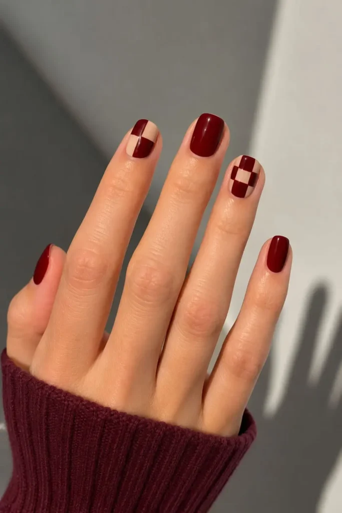 Checkered burgundy nails with dark red grid patterns and negative space
