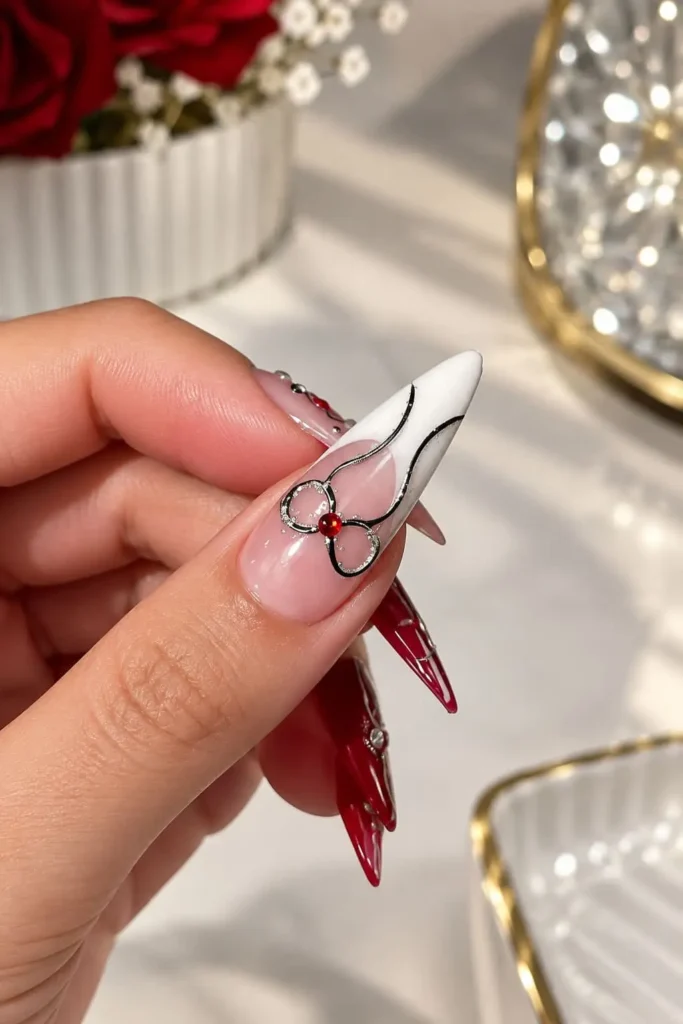 Dainty French tip nails with a silver chrome ribbon and tiny red gem