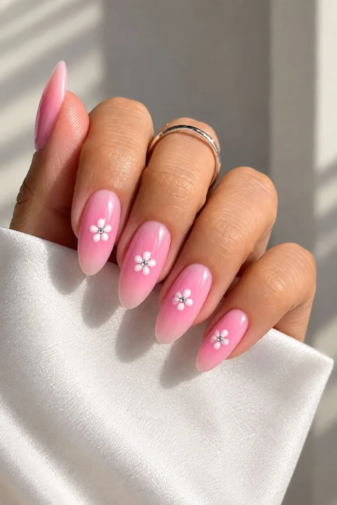 Soft pink aura nails with delicate white daisy charms and crystal accents
